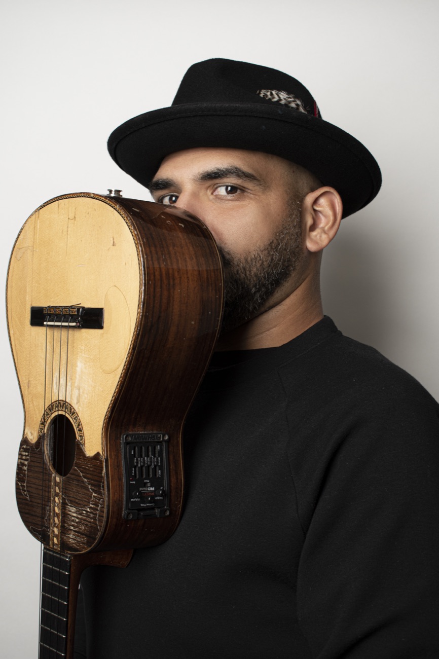 Jorge Glem in a black hat, hiding half of his face behind a cuatro