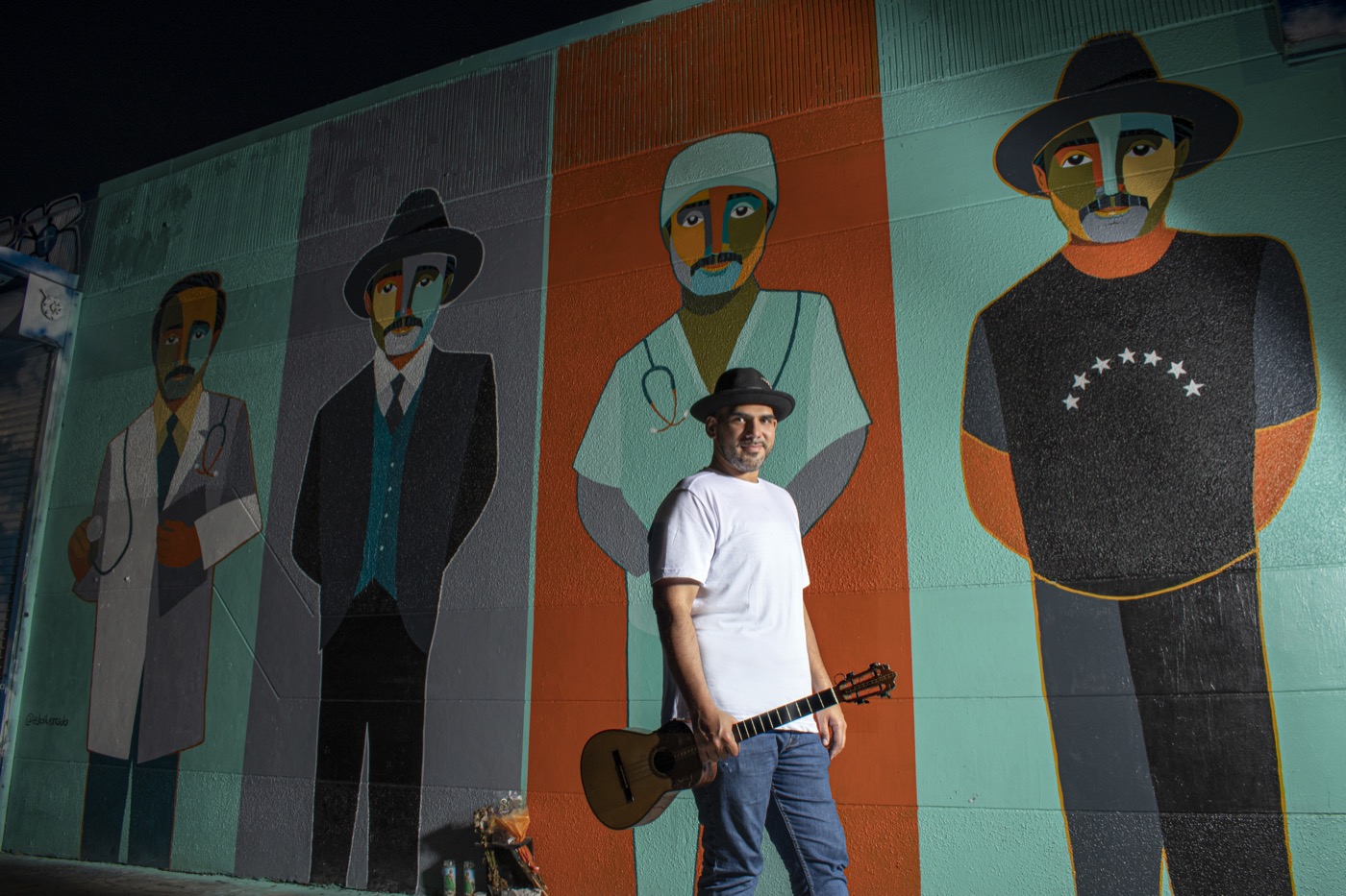 Jorge Glem with his cuatro in front of a mural