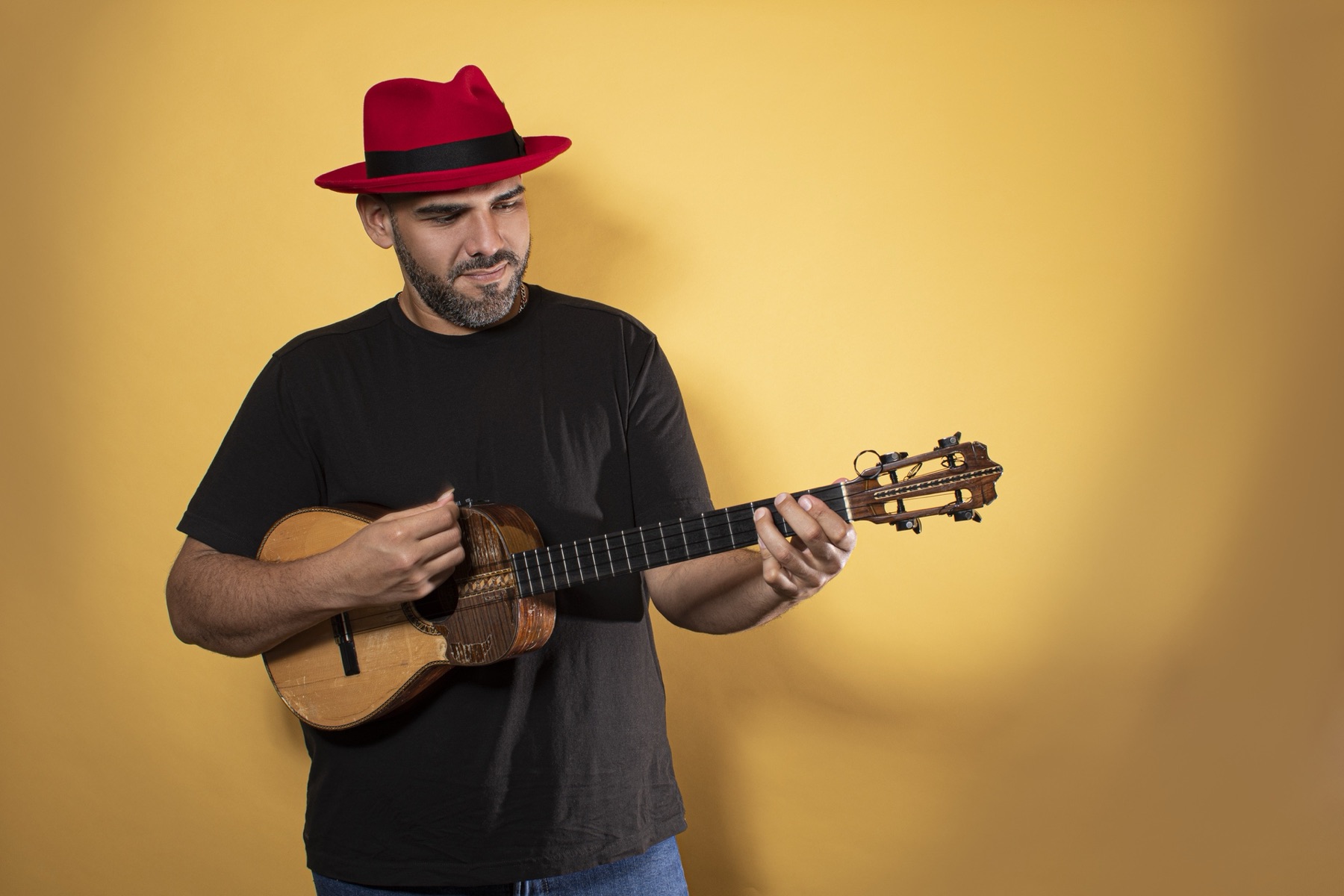 Jorge Glem with a red hat, playing the cuatro against a golden wall