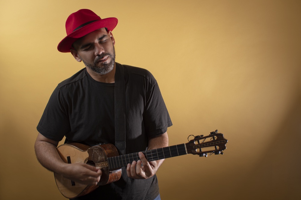 Jorge Glem in a red hat playing the cuatro
